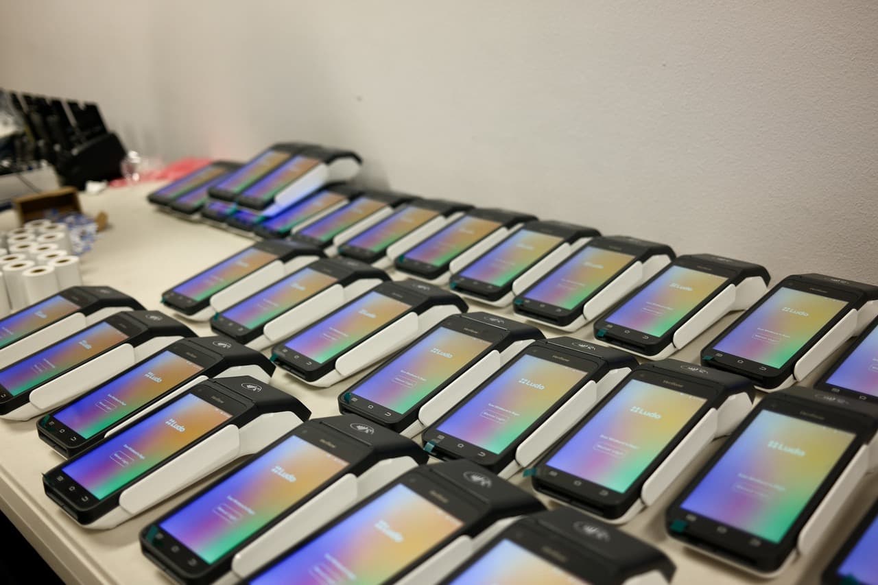 Dozens of Ludo POS terminals lined up on a table, each showing the rainbow Ludo gradient splash screen