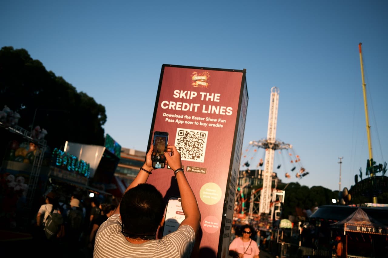 Visitor photographing a "Skip the Credit Lines" QR code sign at the Easter Show